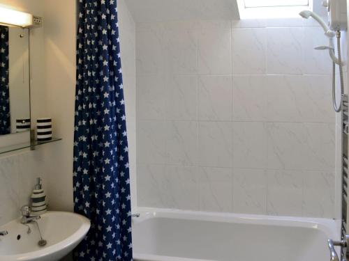 a bathroom with a shower curtain with a tub and a sink at Pottergate Cottage in Wroxham