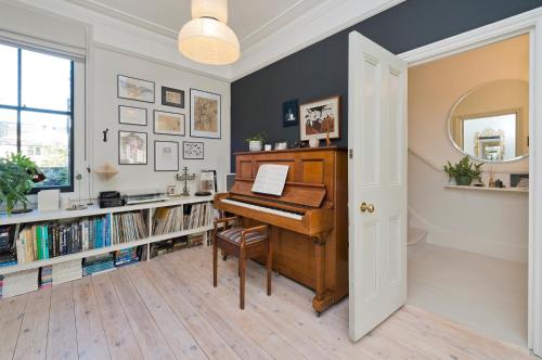 a room with a piano and a book shelf with books at Interior designed house with garden in North West London by UnderTheDoormat in London