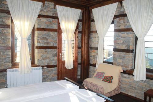 a bedroom with a bed and a chair and windows at Leshtenski Perli in Leshten