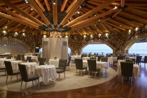 un comedor con mesas y sillas blancas y ventanas en Pelekas Monastery, en Pelekas