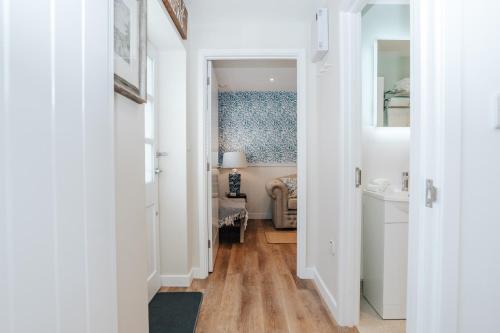 un pasillo que conduce a un dormitorio con paredes blancas y suelo de madera. en Stable Mews, Prestbury Cheltenham, en Southam