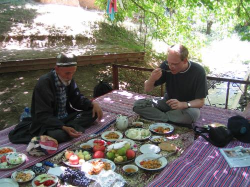 dos hombres sentados en una mesa de picnic con platos de comida en Hayat Guesthouse Nuratau Mountains, en Yukary-Ukhum