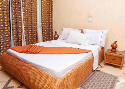 コトヌーにあるAppart'hotel Djembéのベッドルームに籐製のベッド(白いシーツ、枕付)