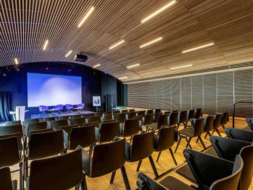 une grande chambre avec des chaises et un écran de projection dans l'établissement Novotel Annecy Centre, à Annecy