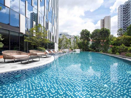 a large swimming pool with chairs next to a building at Novotel Singapore On Stevens in Singapore