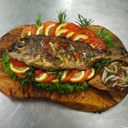 a fish sandwich on a cutting board with vegetables at Cactus Beach Paros in Logaras