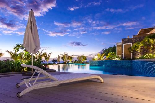 a lounge chair and an umbrella on a deck next to a swimming pool at Cap Ouest Luxury Beachfront in Flic-en-Flac