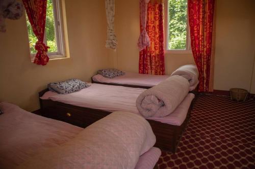 three beds in a room with red curtains at Hasera Organic Farmstay: Farm to Table & Mountain View in Dhulikhel