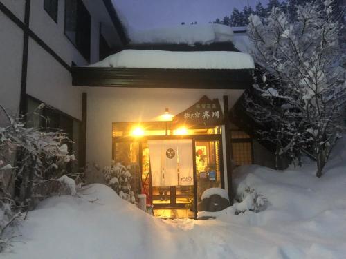 a house covered in snow with a light on the door at Tabinoyado Saikawa in Kuroishi