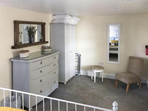 ein Schlafzimmer mit einer Kommode, einem Stuhl und einem Spiegel in der Unterkunft Tiptoe in Steeple Ashton