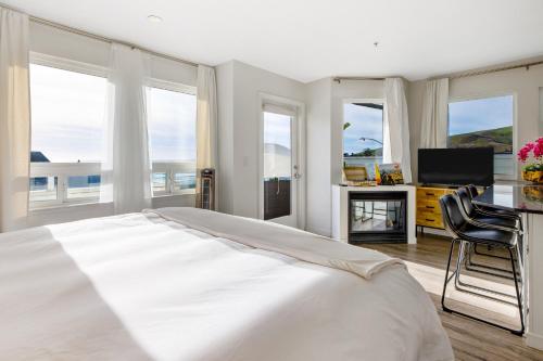 a white bedroom with a large bed and a television at Pier View Suites - Studio B in Cayucos