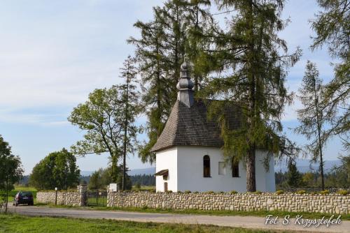Une petite église blanche avec un arbre et une clôture dans l'établissement Nowa Biała Apartament - domek na wyłączność, à Nowa Biała
