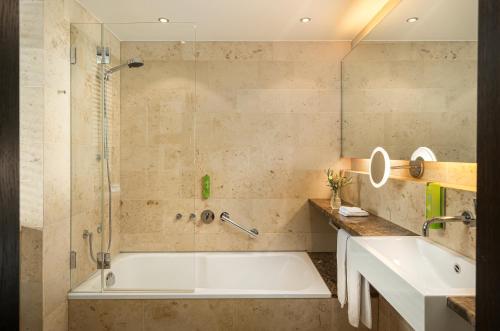 ein Bad mit einer Badewanne, einer Dusche und einem Waschbecken in der Unterkunft Angel's - das hotel am golfpark in Sankt Wendel