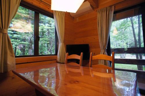 a dining room with a table and chairs and windows at HARUNA CABIN 森の中のログハウス 、広々ウッドデッキでBBQ、公園散策、北軽井沢観光 in Tsumagoi