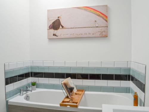 uma casa de banho com uma banheira e uma pintura de pássaros na parede em Garden Cottage em Coldingham
