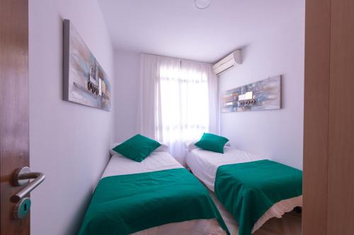 a room with two beds with green sheets and a window at Piso Mirta Santa Cruz Tenerife in Santa Cruz de Tenerife
