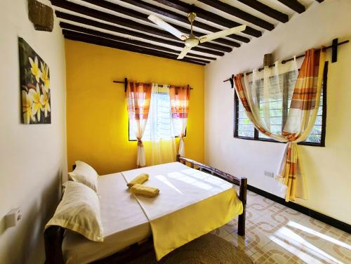 a bedroom with a bed with yellow walls and windows at Frangipani House Nungwi Zanzibar in Nungwi