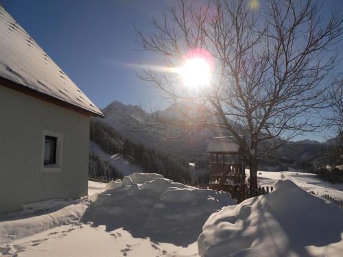 a snow covered house with the sun shining behind a tree at Familienbauernhof Imitz, Ferienwohnung in Spital am Pyhrn