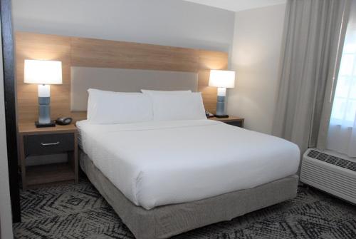 a white bed in a hotel room with two lamps at Candlewood Suites Tallahassee by IHG in Tallahassee