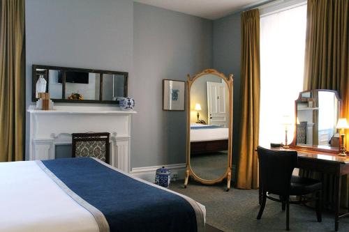 1 dormitorio con cama, escritorio y espejo en The Priory Hotel, en Pittsburgh