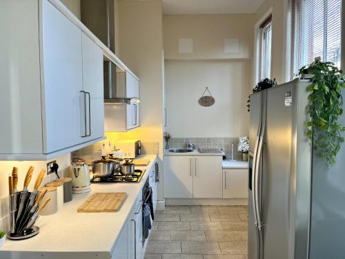 uma cozinha com armários brancos e um frigorífico de aço inoxidável em City Link - Mapperley Park Suite - Free parking,tram&busroutes,HSwifi,upto9 by KP em Nottingham