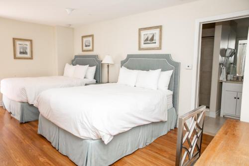 two beds in a bedroom with white walls and wood floors at Three Village Inn in Stony Brook