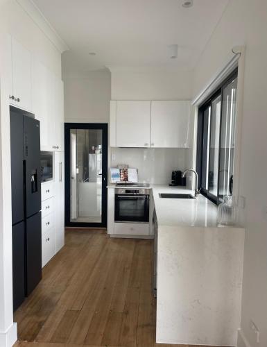 a kitchen with white cabinets and a black refrigerator at 4BR Waterfront - Skippers Quarterdeck in Lakes Entrance