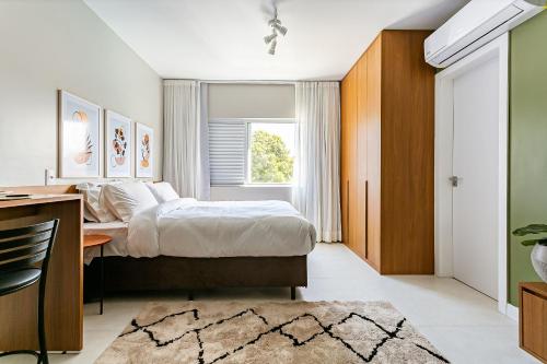 a bedroom with a bed and a desk and a window at Predio com apartamentos completos, com piscina e a passos da praia - Agua Marinha in Florianópolis