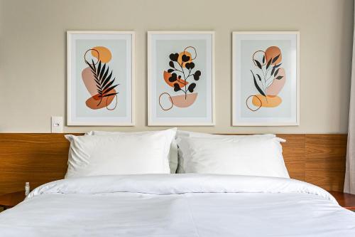 three pictures of flowers on the wall above a bed at Prédio com apartamentos completos, com piscina e a passos da praia - Agua Marinha in Florianópolis