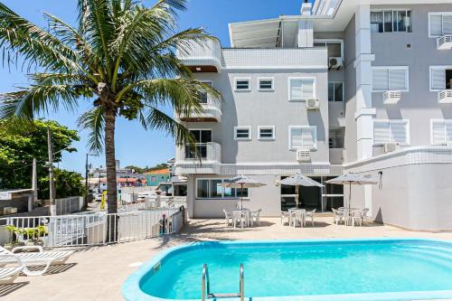 a swimming pool in front of a building with a palm tree at Prédio com apartamentos completos, com piscina e a passos da praia - Agua Marinha in Florianópolis