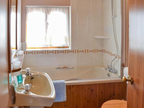 een badkamer met een bad, een wastafel en een raam bij Merlin View in Saint Mawgan