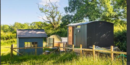 a tiny house and a shed in a field at Shepherds Hut with Scandinavian Hot Tub and hydromassager in Sway
