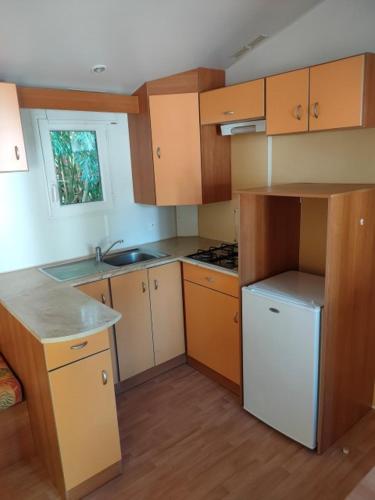 Elle comprend une petite cuisine avec des placards en bois et un réfrigérateur blanc. dans l'établissement CAMPING LE BEL AIR mobil home LE CORNOUILLER 4 personnes, à Limogne-en-Quercy