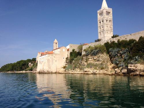 a castle with a clock tower on a hill next to the water at Guesthouse Tariba in Supetarska Draga