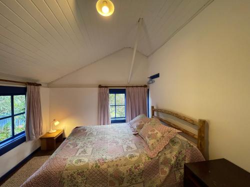 a bedroom with a bed and two windows at Hospedaria Fazenda São João do Vale da Grama in Visconde De Maua