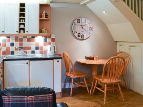 a kitchen with a table and chairs and a clock on the wall at Larch Cottage in Craster