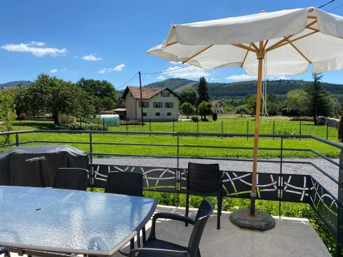 a table and chairs with an umbrella and a field at Les Catèdjes in Fraize