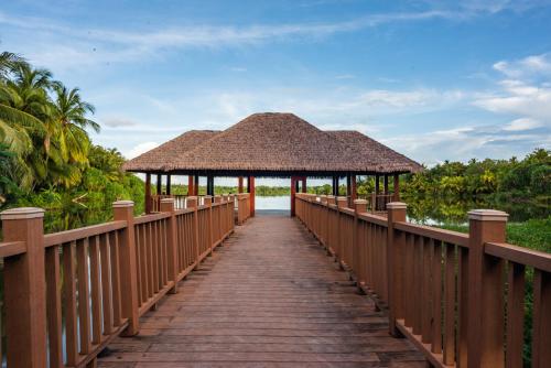 a wooden boardwalk leading to a resort with a thatch roof at Isle Royal Inn in Fuvahmulah