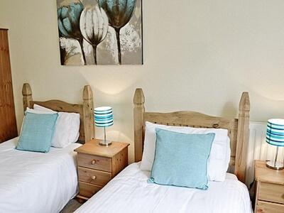 a bedroom with two beds with blue and white pillows at Cartmel Cottage in Lindale