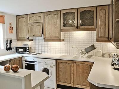 a kitchen with wooden cabinets and a white dishwasher at Cartmel Cottage in Lindale