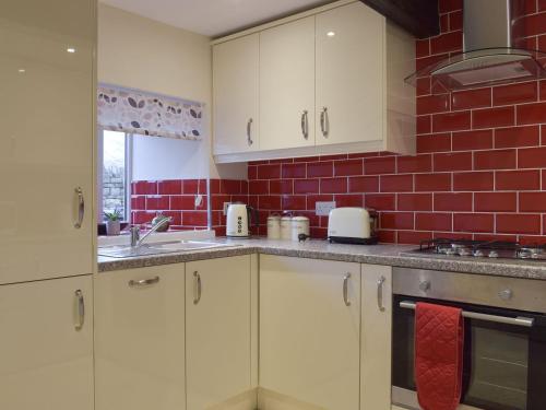 a kitchen with white cabinets and a red brick wall at Rosemount Cottage in Salterforth