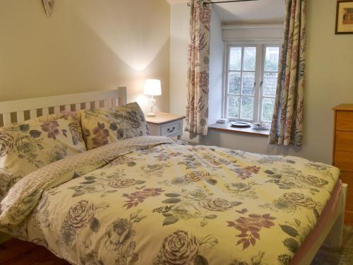 a bedroom with a bed with a floral bedspread and a window at Blackberry Cottage in Kenton