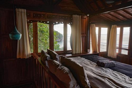 ein großes Bett in einem Zimmer mit Fenstern in der Unterkunft The Hidden Escapes- Unique Tiny Home on Bingin Beach with Breathtaking Ocean & Sunset Views in Uluwatu
