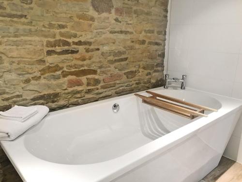 a white bath tub in a bathroom with a brick wall at The Old Cow Shed in Barlow
