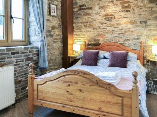a bedroom with a wooden bed and a stone wall at The Old Cow Shed in Barlow