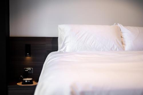 un letto con cuscini bianchi e una sveglia su un tavolo di And Apartments a Canberra