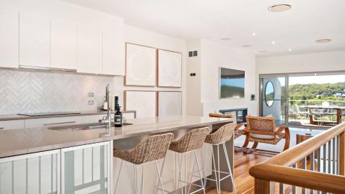 a kitchen with white cabinets and a bar with chairs at Coast Fingal Bay in Fingal Bay