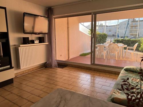 un salon avec une télévision et une terrasse avec une table dans l'établissement Grand 3 Pièces avec Terrasse, Lave-Linge et Lave-Vaisselle, Animaux Acceptés - FR-1-702-24, au Cap d'Agde