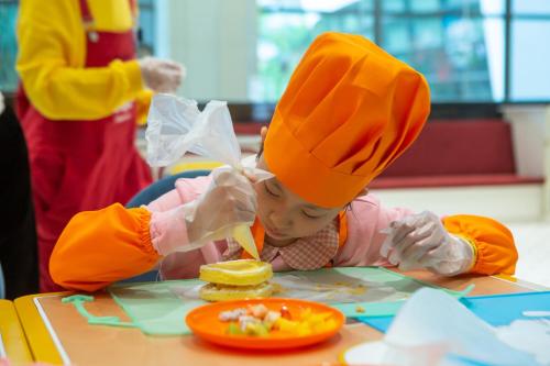 InterContinental Shenzhen, an IHG Hotel في شنجن: طفل يرتدي قبعة شيف يأكل الطعام على طاولة