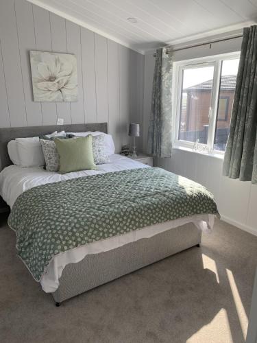 a bedroom with a bed with a green comforter and a window at Cherry Blossom 42 Hot Tub in Garton